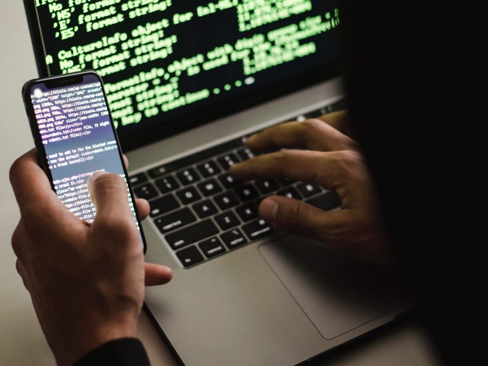 Free Unrecognizable hacker with smartphone typing on laptop at desk Stock Photo